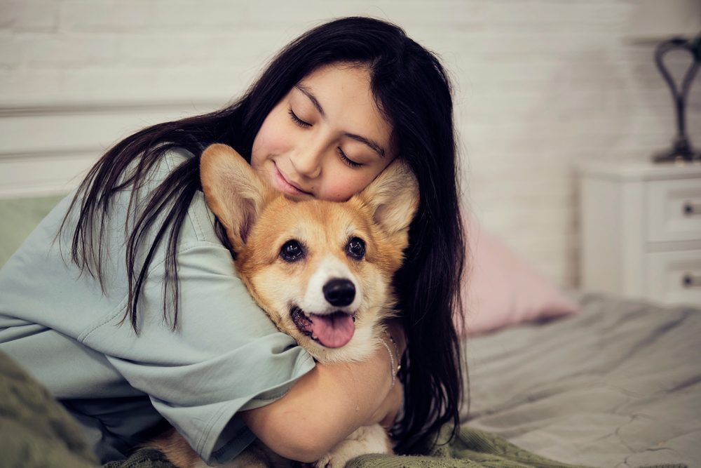 woman hugging corgi in bed